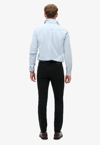 Jasnoniebieska koszula z długim rękawem i wysokim kołnierzem, zestawiona z obcisłymi czarnymi dżinsami. Koszula ma długie rękawy i jest włożona w spodnie.