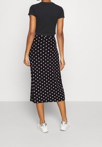 Jupe midi noire à pois blancs, tissu lisse, design légèrement évasé, associée à un haut noir à manches courtes et des baskets argentées.