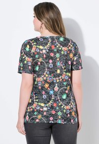 Černé tričko s krátkým rukávem, které má multikolorový potisk s drahými kameny. Materiál vypadá jemně; design zahrnuje květinové a gemové tvary po celém povrchu.