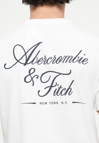 White cotton t-shirt featuring large black text reading "Abercrombie & Fitch" and "NEW YORK, N.Y." on the back. Rounded neckline, short sleeves.