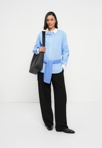 Ανοιχτό μπλε πουκάμισο με λευκό γιακά, μαύρο παντελόνι με φαρδιά πόδια και μπλε πουλόβερ δεμένο στη μέση, συνοδευόμενο από μαύρη τσάντα tote.