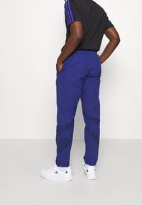 Pantaloni sportivi blu con accenti neri a motivo, vita elastica, tasche e caviglie a costringere, abbinati a sneakers bianche.