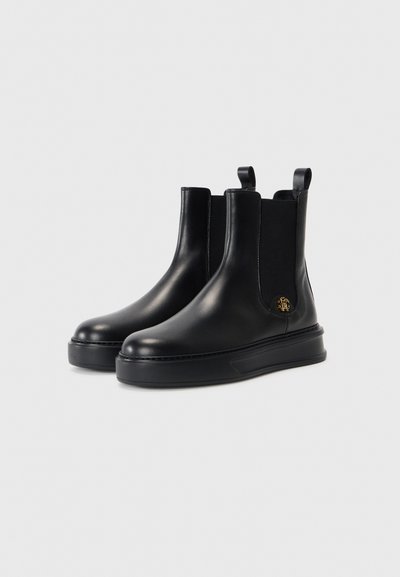Svarta läderankelboots med elastiska sidopaneler, platta sålar och en liten logotypdetalj. Slät yta och rund tådesign.
