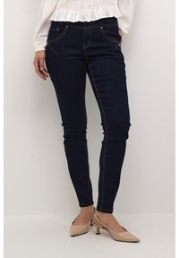 Hubené tmavě modré džíny z denimu, se zlatými švy, předními kapsami na zip, v kombinaci s nahými lodičkami na podpatku.