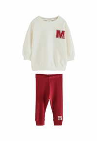 Krém színű pulóver kapucnis felső, piros "M" logóval, piros leggings-szel párosítva. Puha anyag, laza fazon, bordázott mandzsetták és textúrált részletek.