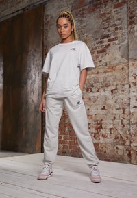 T-shirt oversize grigio chiaro e jogger coordinati, entrambi realizzati in tessuto morbido e testurizzato. Presenta un logo ricamato sul petto e sulla gamba del pantalone.