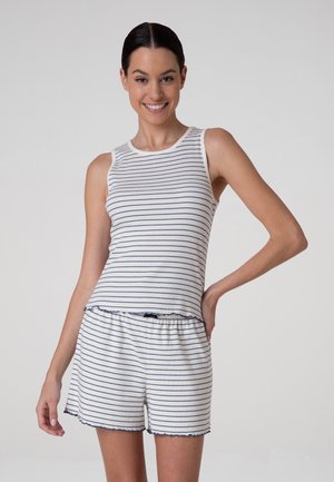 Donna sorridente con capelli scuri che indossa un top bianco senza maniche e pantaloncini abbinati con sottili righe orizzontali blu navy.
