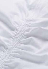 Witte stof met een geplooid textuur, met een geraffineerde naad die door het middenloopt. Gladde, zachte textuur met een schoon, minimalistisch ontwerp.