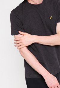 Czarnoszary T-shirt z krótkim rękawem wykonany z bawełny, z małym żółtym logo na klatce piersiowej. Gładka struktura, okrągły dekolt i dopasowany krój.