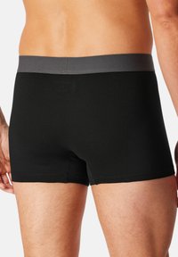 Schwarze Baumwoll-Boxershorts mit einem grauen elastischen Bund, die eine glatte Textur und ein körpernahes Design aufweisen und die Rückansicht zeigen.