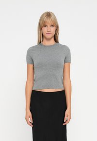 Haut en tricot gris, à manches courtes et taille courte, avec un col rond. Texture douce, design minimal, associé à une jupe noire.