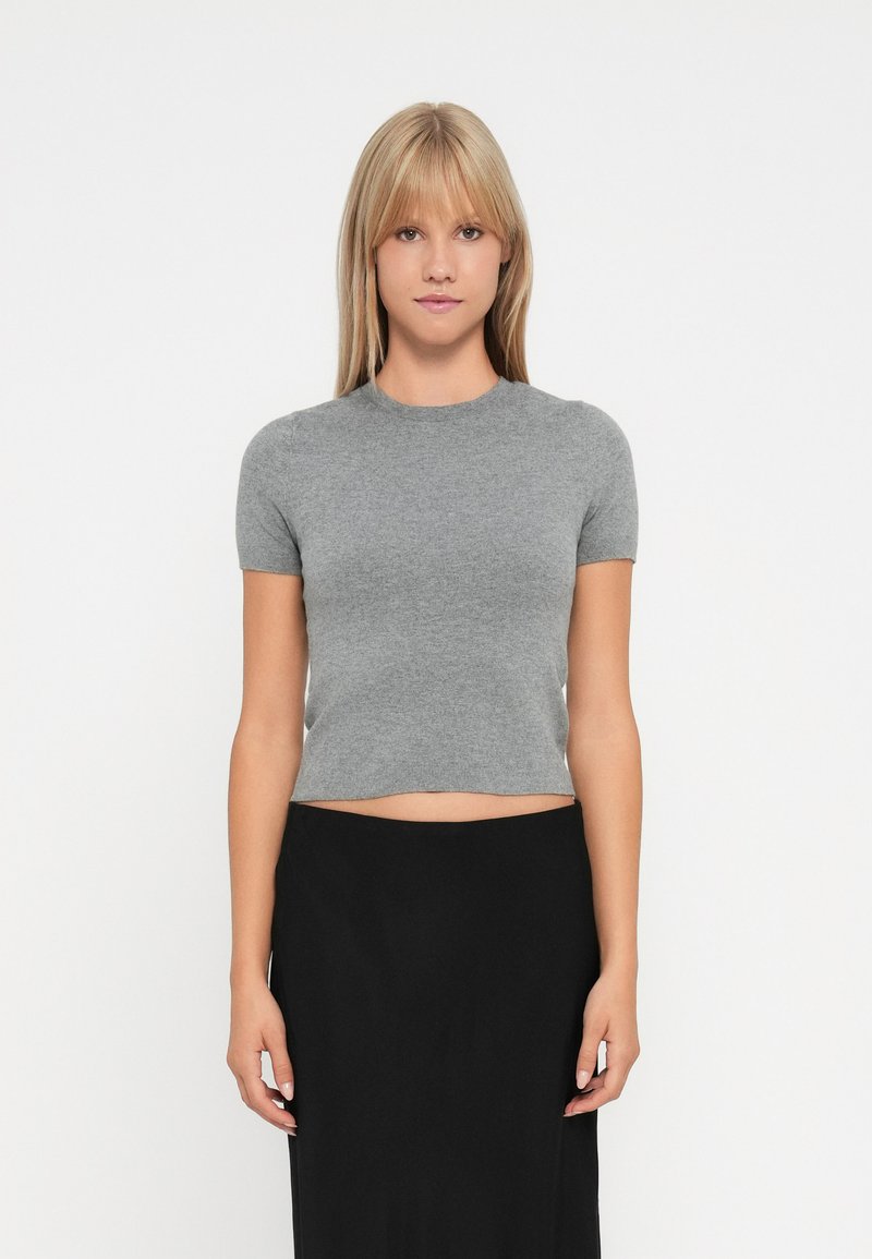 Haut en tricot gris, à manches courtes et taille courte, avec un col rond. Texture douce, design minimal, associé à une jupe noire.