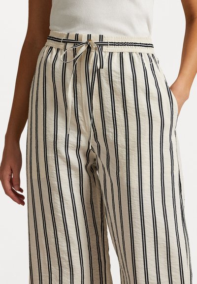 Pantalons rayés crème avec des lignes verticales noires, dotés d'une taille élastique avec cordon de serrage et poches latérales. Tissu texturé.