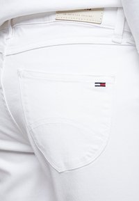 Vaqueros de mezclilla blanca que cuentan con un bolsillo trasero con un diseño curvado sutil y un pequeño logo bordado en rojo, blanco y azul.