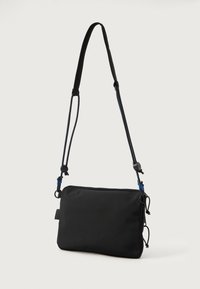 Sort rektangulær taske med lynlås, justerbar rem og blå detaljer. Har slidstærkt materiale og to side snoretræk til design.