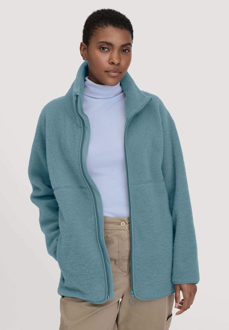 Giacca in pile azzurro chiaro con colletto alto, zip completa e due tasche frontali. Presenta una texture morbida e una vestibilità rilassata e oversize.