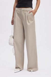 Pantaloni beige a gamba larga in un morbido tessuto, con un design plissettato e tasche laterali. Abbinati a una piccola borsa bianca decorata con perline e scarpe con punta.