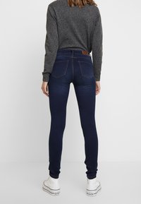 Tunna mörkblå jeans med hög midja, med bakfickor, och kombinerade med vita hög-top snörskor och en grå långärmad tröja.