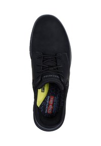 Baskets slip-on noires Skechers avec lacets noirs, col rembourré, et semelle intérieure jaune et noire arborant un texte de marque.