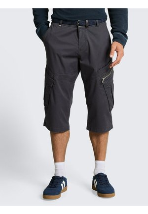 Man draagt donkergrijze cargoshorts tot op de knie, marineblauwe sneakers met witte strepen, witte sokken en een donker shirt met lange mouwen.