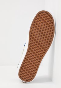 Suola di sneaker bianca caratterizzata da una suola in gomma marrone texturizzata con un motivo a diamante, bordo piatto e elementi di design laterali minimi.