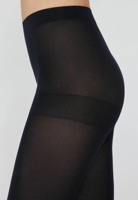 Leggings neri opachi con una texture liscia, caratterizzati da una ampia cintura elastica e una silhouette aderente, progettati per comfort e flessibilità.