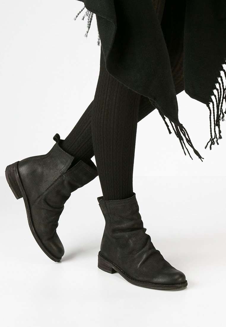 Bottines en cuir noir avec un design décontracté, surface texturée et un petit talon en bois. Portées avec des collants noirs à motifs.