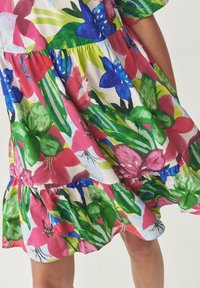 Bloemige jurk met een kleurrijk patroon van grote roze, blauwe en groene bloemen. Het materiaal is lichtgewicht met een gelaagde, gerimpelde zoom.