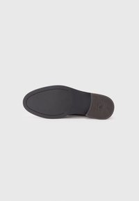 Semelle de chaussure noire avec une surface lisse et texturée, et une silhouette ovale. Présente un motif près du talon pour une bonne adhérence.