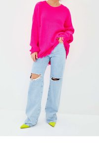 Pink, oversized, textured knit sweater paired with distressed, light blue wide-leg jeans featuring large rips; bright green pointed toe heels.