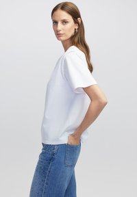 Witte t-shirt met korte mouwen en een relaxte pasvorm, voorzien van studdetails op de schouder en gecombineerd met blauwe spijkerbroek.