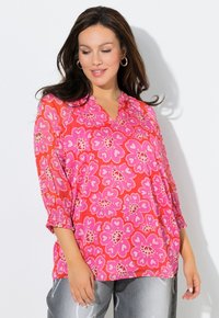 Różowa kwiatowa bluzka z dekoltem w kształcie litery V, r�ękawami do połowy przedramienia i marszczonymi mankietami. Ozdobiona dużymi, sercowatymi kwiatami w różnych odcieniach różu.