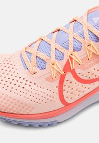 Scarpe da corsa rosa chiaro con accenti arancioni, tomaia in rete e texture traspirante. Presentano una linguetta imbottita e dettagli riflettenti.