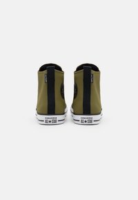 Zelené plátěné vysoké tenisky s černými akcenty a bílou gumovou podrážkou. Obsahují logo Converse na boku a kontrastní patní tab.