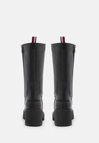 Bottes en cuir noir montantes avec un talon épais, dotées d'une fermeture éclair sur le côté et d'une tirette rouge, blanche et bleue en haut.