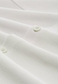 Witte textuurstof met zichtbare ribbels, met verschillende knopen die op het oppervlak zijn genaaid, in een overlappende stijl gerangschikt.