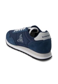 Navy blue sneaker made of suede and synthetic material, featuring white laces, a padded collar, and a logo on the side. Rubber sole.
