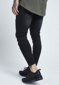 Svarta smala jeans med en slitstark yta, i kombination med svarta atletiska sneakers med en texturerad mesh-övre och synlig dämpning.