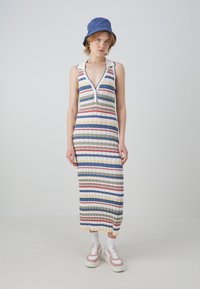 Vestido a rayas, hasta la rodilla, con escote en V y tapeta de botones. Hecho de tela acanalada en patrones horizontales multicolores. Combinado con zapatillas blancas.