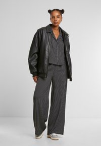 Giacca nera in pelle oversize indossata sopra una blusa a righe bianco e nera e pantaloni a gamba larga. Sneakers grigie con suola chiara.