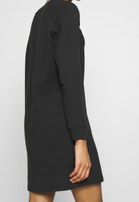 Robe noire à manches longues avec un col rond et des manches avec poignets, confectionnée dans un tissu doux et lisse avec une coupe décontractée.