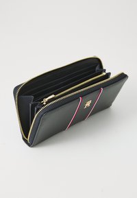 Navy leather wallet with gold zipper, featuring multiple card slots and a red and white accent stripe. Embossed logo on the front.