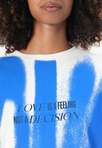 Blue and white graphic sweatshirt with soft texture. Features bold black text: "LOVE IS A FEELING NOT A DECISION" in a modern font.
