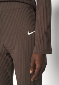 Bruna ribbade leggings med en vit Nike-logotyp. Hög midja och åtsittande passform, som framhäver texturerad tyg och subtila sömdetaljer.