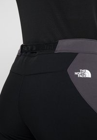 Mustat urheiluleggingsit harmaalla vyötäröllä ja kaarevalla harmaalla aksentilla sivussa. Sisältää valkoisen "The North Face" -logon. Sujuva pinta.
