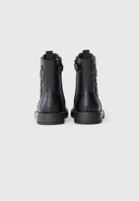 Schwarze Stiefeletten aus glattem Leder mit Reißverschluss und einem strukturierten Blumendesign an der Außenseite. Flache Gummisohlen.