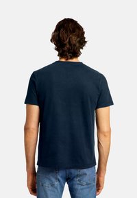 Marineblaue kurzärmelige T-Shirt mit rundem Ausschnitt und glatter Textur, getragen von einer Person mit hellen Jeans.