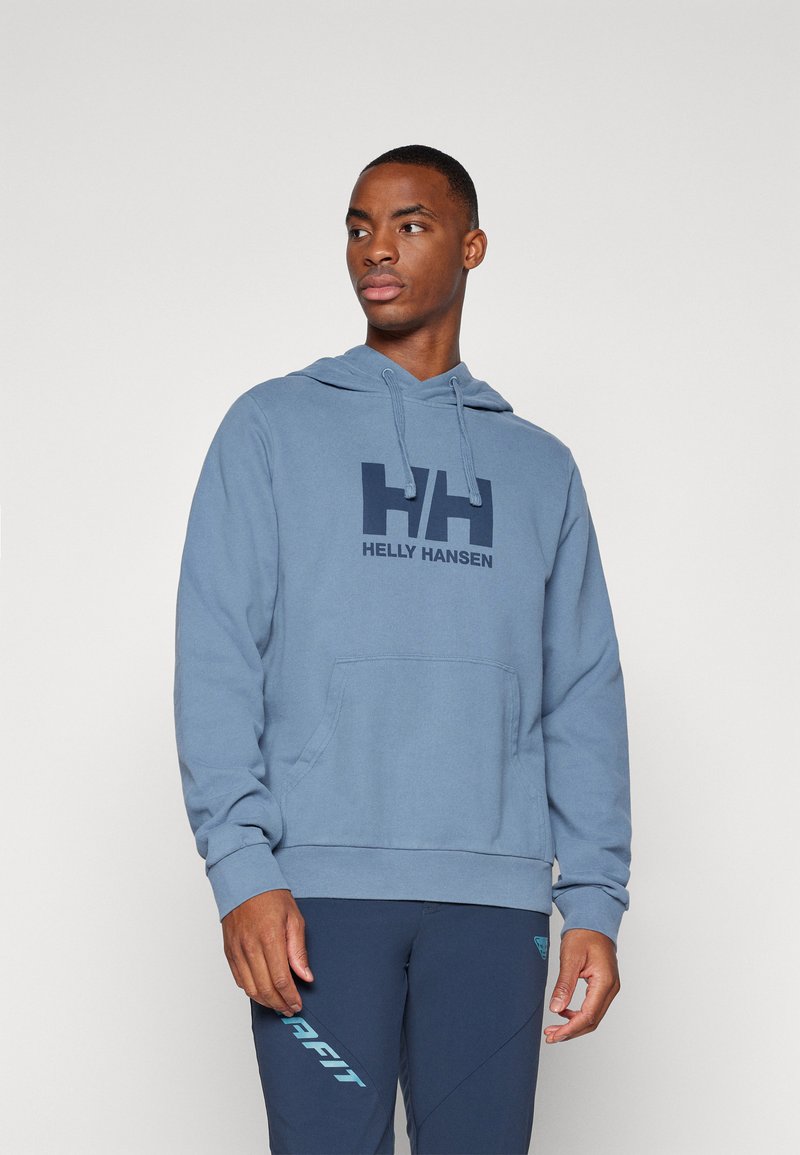 Felpa blu con tasca frontale, cappuccio con cordino e logo Helly Hansen blu scuro. Il tessuto appare morbido, con polsini e orlo a coste.