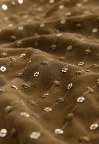 Brunt stof med lodrette rækker af små skinnende palietter og teksturerede stingprikker, der skaber et hævet, bølget mønster.