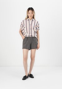 Kurzarm-Hemd mit roten und blauen Streifen, kombiniert mit grauen Shorts. Das Outfit hat eine entspannte Passform und Knopfdetails.